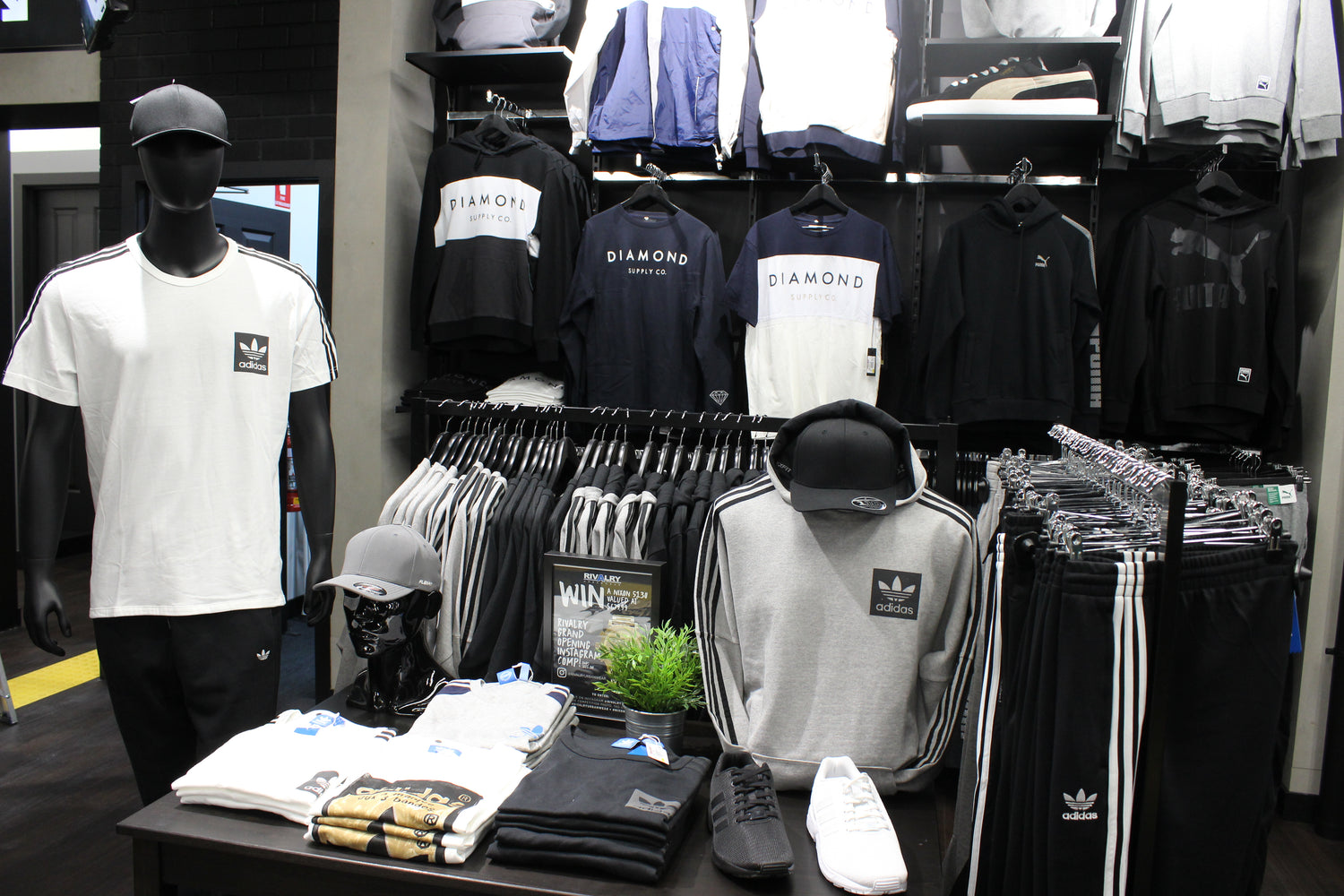 Display of clothing and accessories in a store with mannequins and racks.