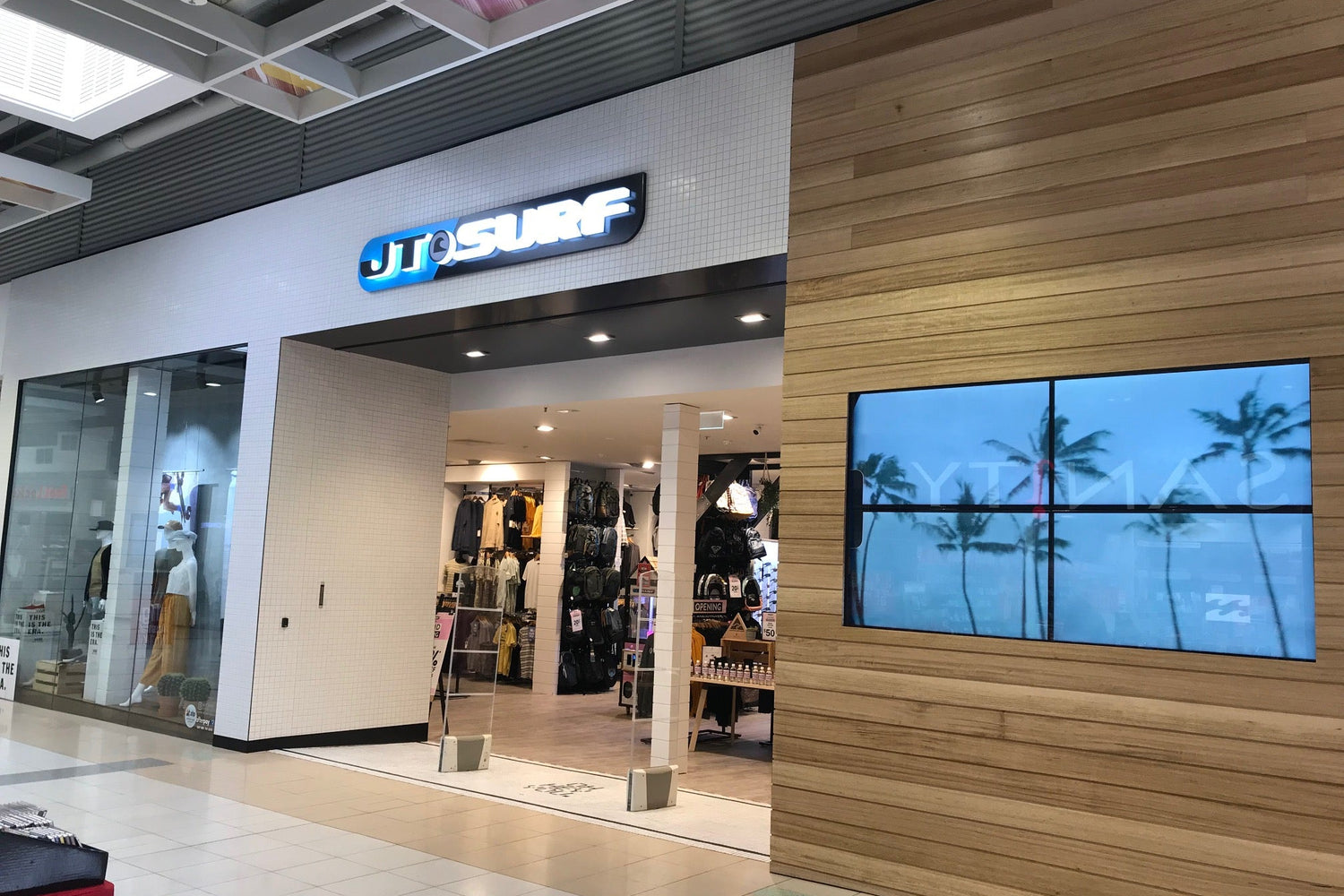Storefront of a clothing store with a wooden wall and screen displaying palm trees.
